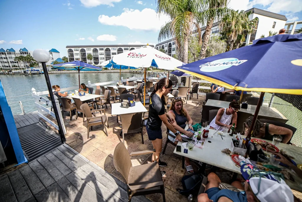 Sunny outdoor restaurant patio with people eating by the water.