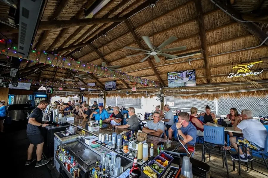 Tiki bar interior with thatched roof, string lights, bartender, and patrons.