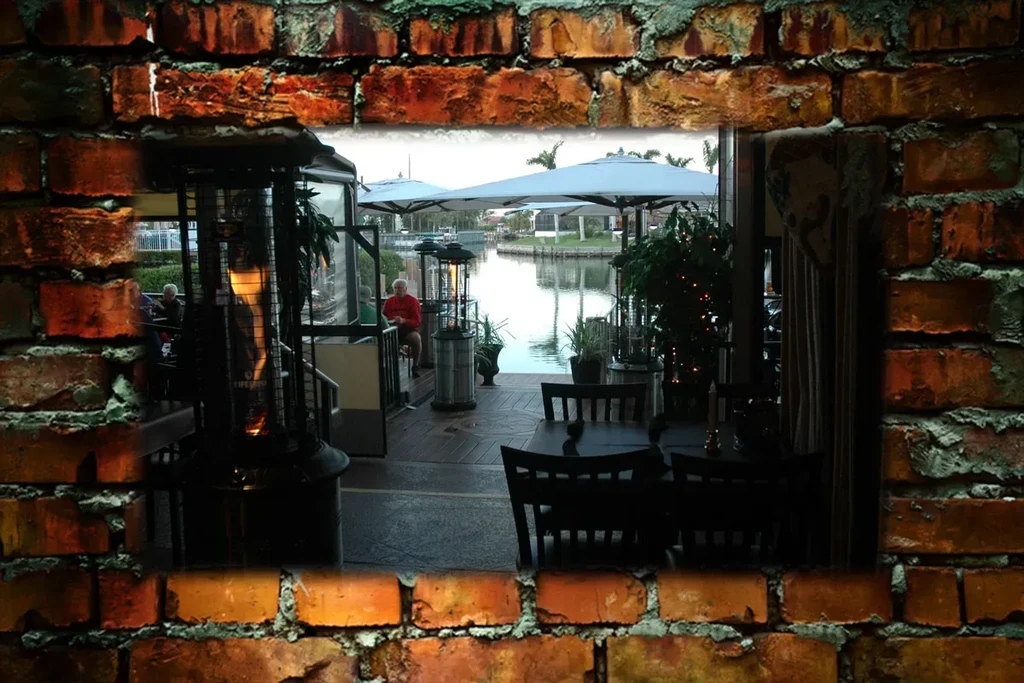 Rustic brick frame reveals a dimly lit waterside restaurant with people.