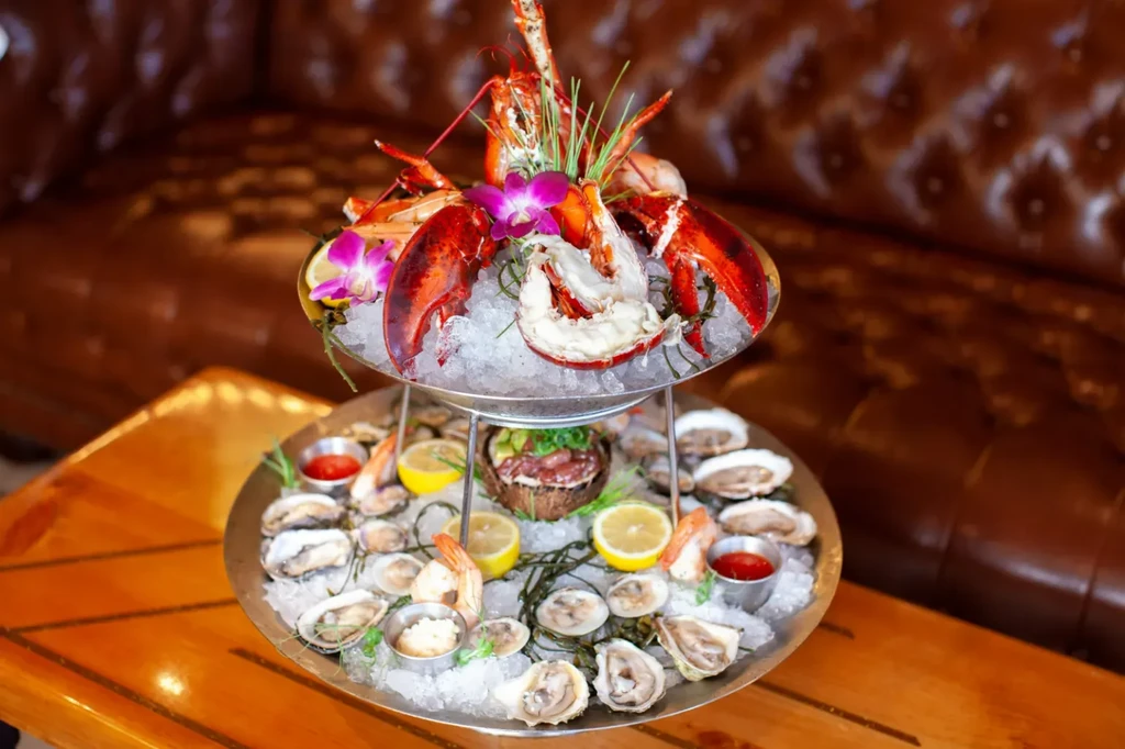 Multi-tiered seafood tower with lobster, oysters, shrimp, sauces, and orchids.