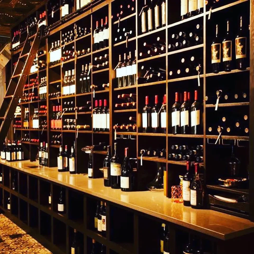 Extensive wine display wall with tall wooden shelves, counter, and rolling ladder.
