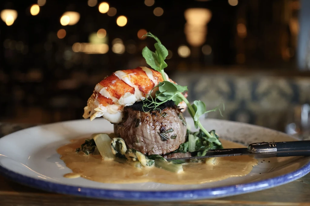 Plated steak, lobster tail, green vegetables, and creamy sauce.