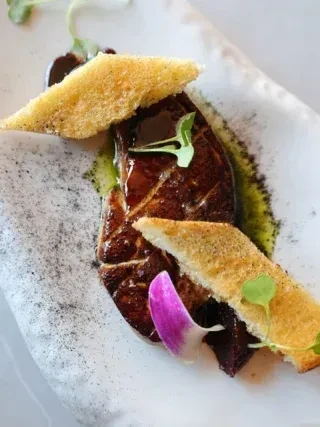 Seared gourmet dish plated with toast, green sauce, microgreens, flower.