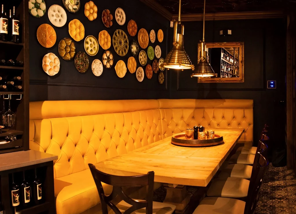 Upscale restaurant with long wooden table, mustard-yellow booth, and decorative wall plates.