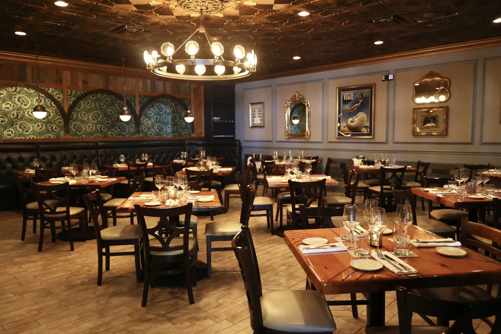 Elegant, empty restaurant with set tables, banquettes, and chandeliers.
