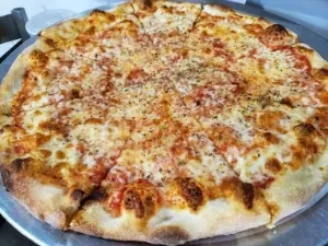 Whole baked pizza with melted mozzarella and herbs on a silver tray.