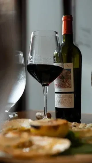 Close-up of a DiMares red wine glass, bottle, and food dishes.