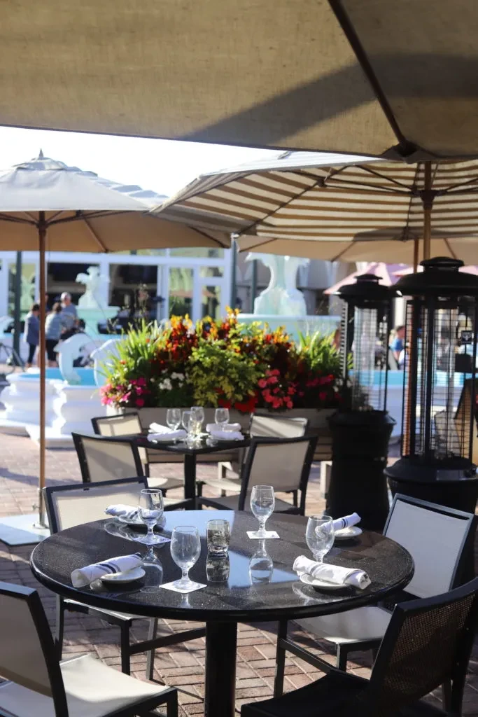 Outdoor dining patio with shaded tables, flowers, and a fountain.