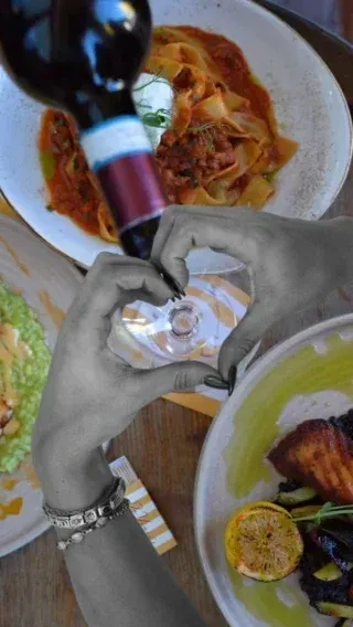Overhead shot of colorful food and wine being poured by grayscale hands.