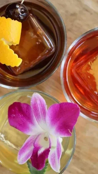 Three distinctly garnished drinks in clear glasses on a wooden surface.