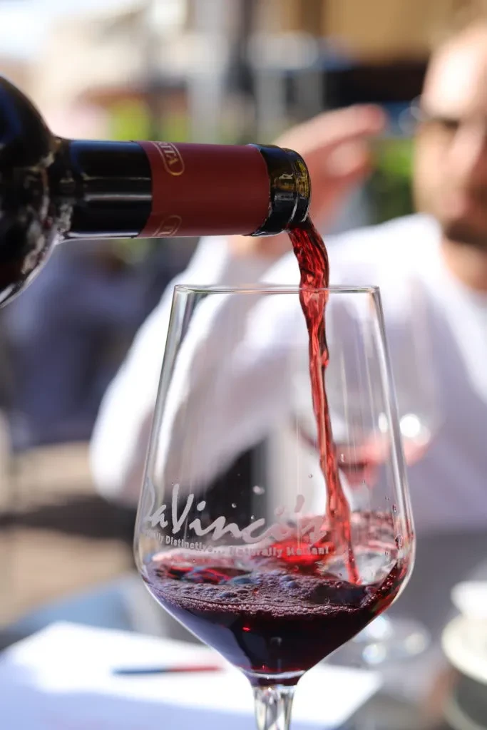 Close-up: Red wine pours from a dark bottle into a clear glass.