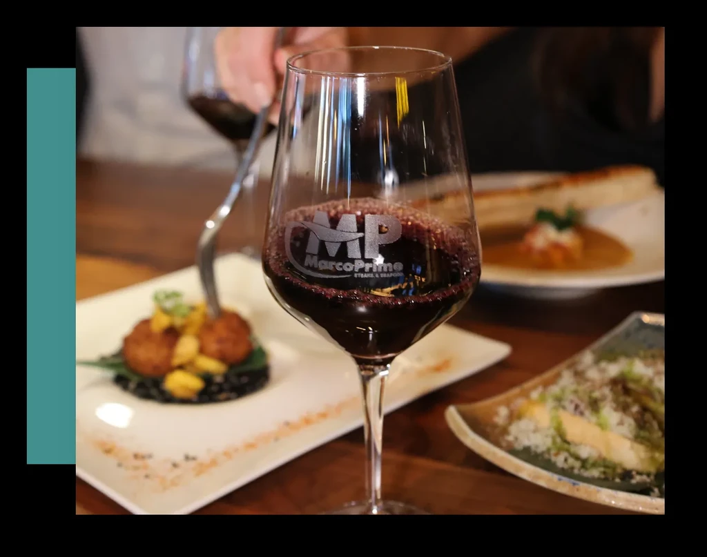 Etched MarcoPrime wine glass, fried food, and a hand with a fork.