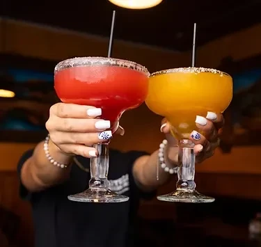 Two hands holding red and yellow frozen margarita glasses.