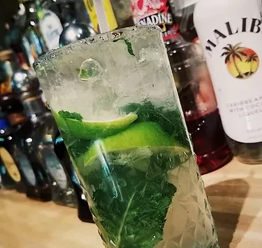 Close-up mojito cocktail with lime, mint, and ice in a bar setting.