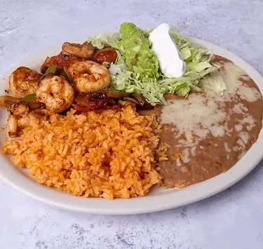 Plate of Mexican food with shrimp fajitas, rice, beans, and guacamole.