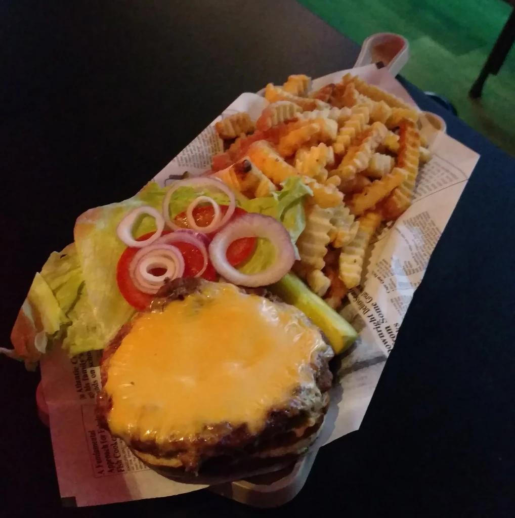 Hamburger, crinkle-cut fries, and pickle spear on a newspaper-lined tray.