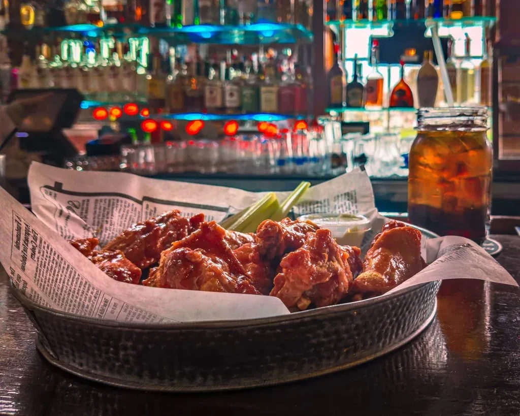 Sauced chicken wings, celery, and iced drink on a blurred bar.