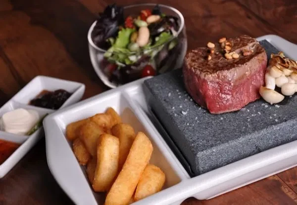 Medium-rare steak on hot stone with fries, sauces, and green salad.