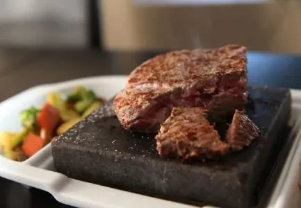 Steaming medium-rare steak on a hot stone with vegetables.