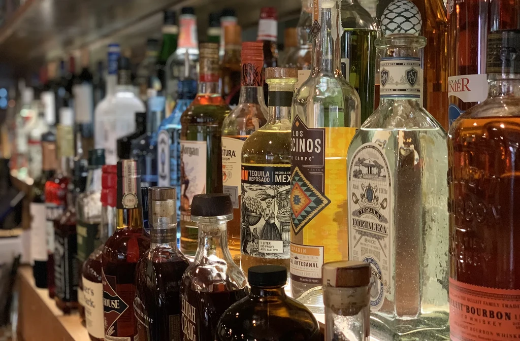 Well-stocked bar shelf displaying bottles of tequila, whiskey, bourbon, and mezcal.