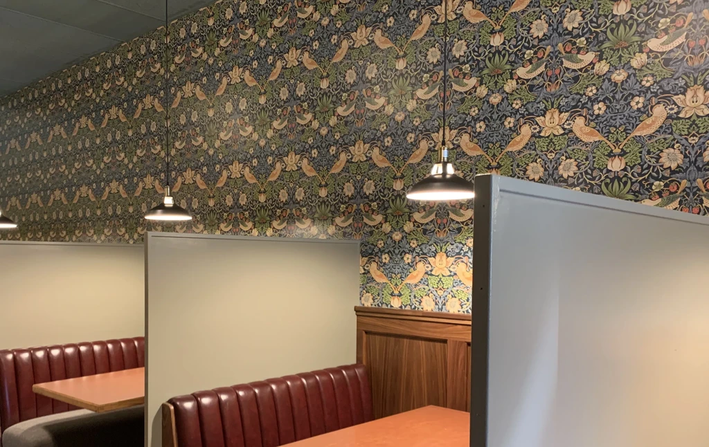 Restaurant interior with patterned wallpaper, booth seating, and pendant lights.