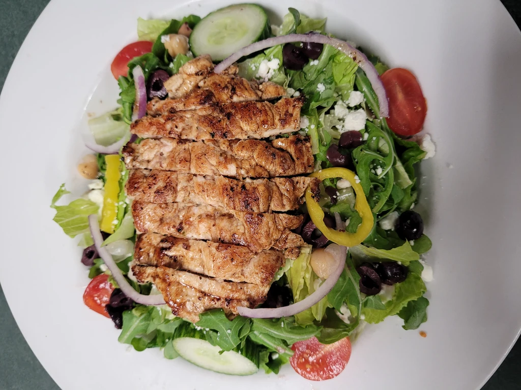 Overhead view of grilled chicken salad with mixed greens and vegetables.