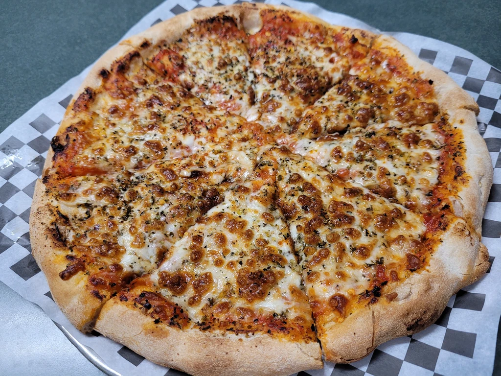 Sliced pizza with melted cheese and herbs on checkerboard paper.
