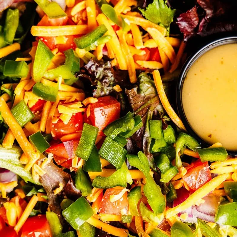 Overhead close-up of salad with lettuce, peppers, tomatoes, cheese, and dressing.