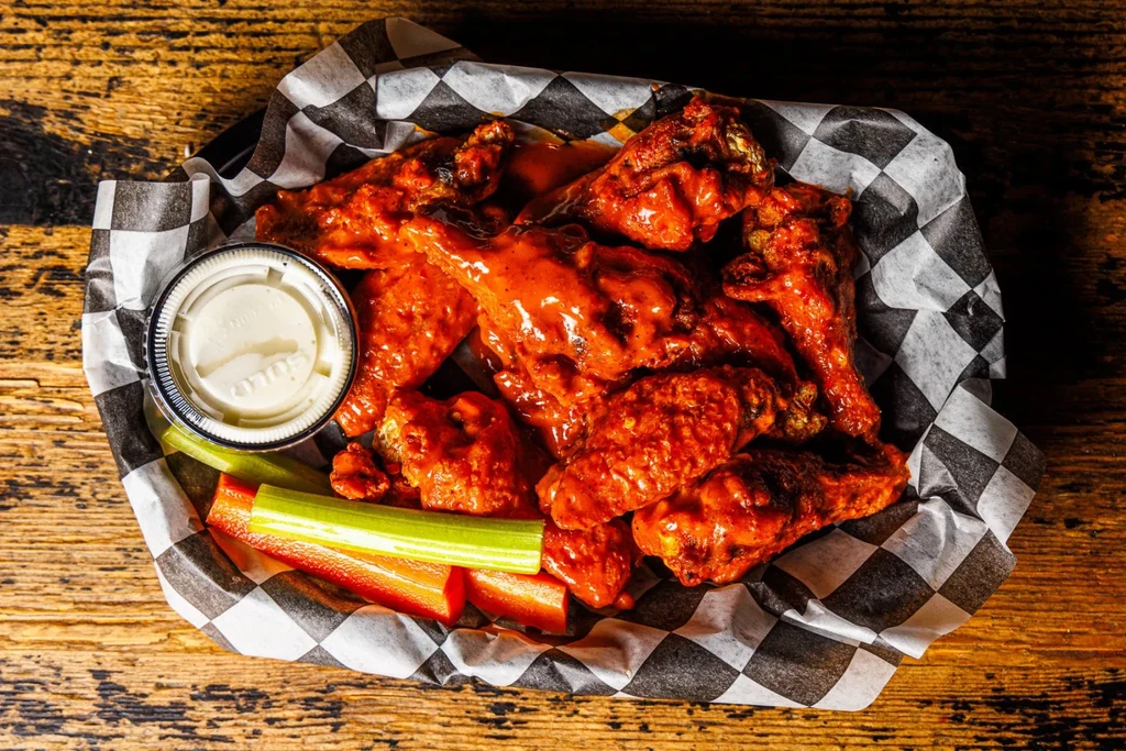 Generous buffalo wings, celery, carrots, and dip in a basket.