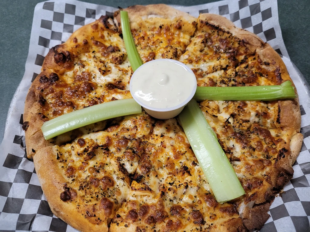 Overhead: Cheesy bread wedges, creamy dip, and celery on checkered paper.