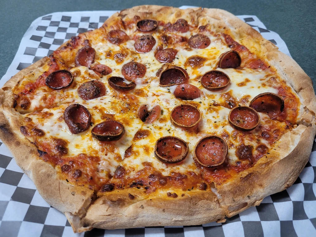 Whole pepperoni pizza with melted cheese on checkerboard deli paper.