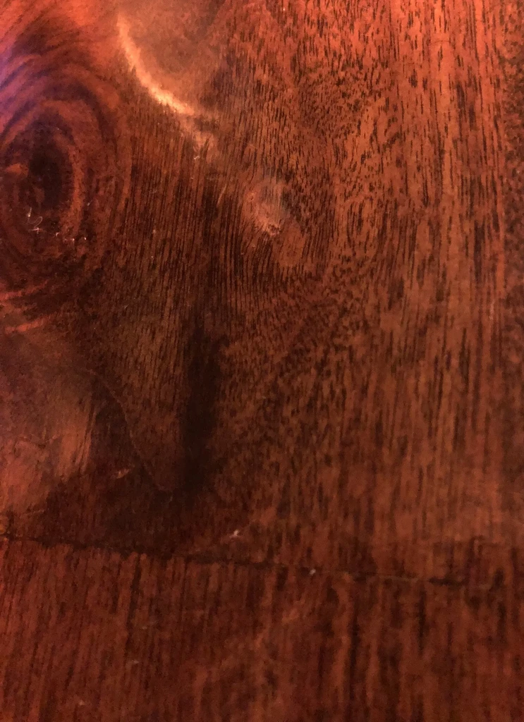 Warm reddish-brown wooden surface, close-up with intricate grain and knot.