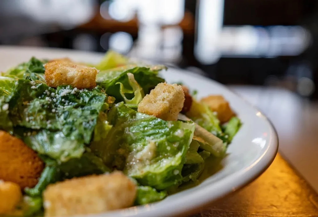 Caesar salad in a white bowl with romaine, Parmesan, and croutons.