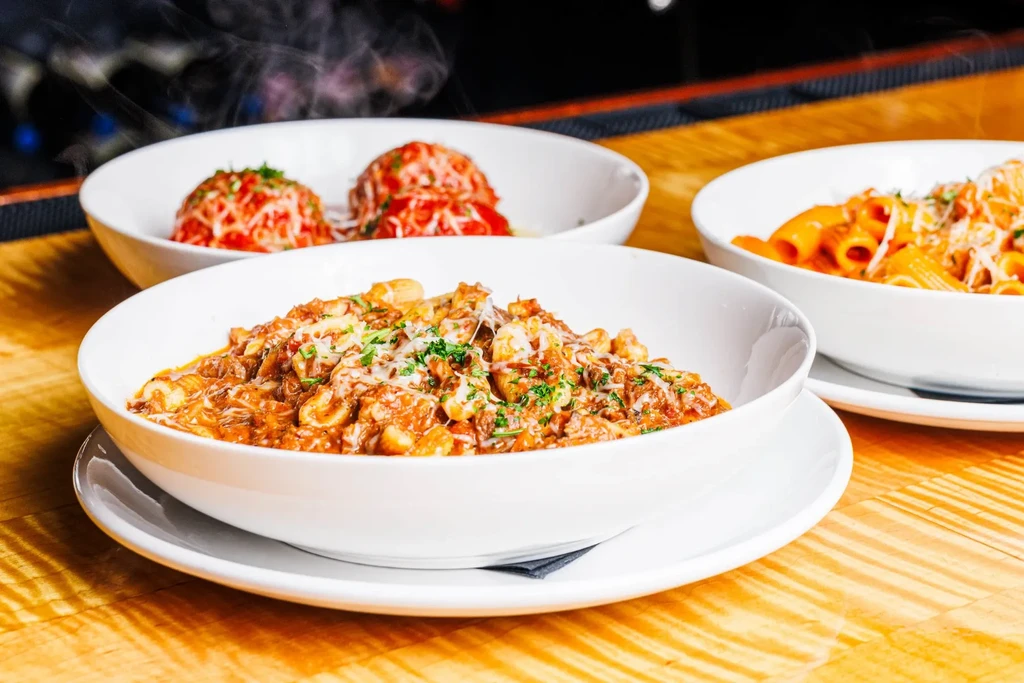 Three steaming bowls of pasta with cheese on a wooden table.