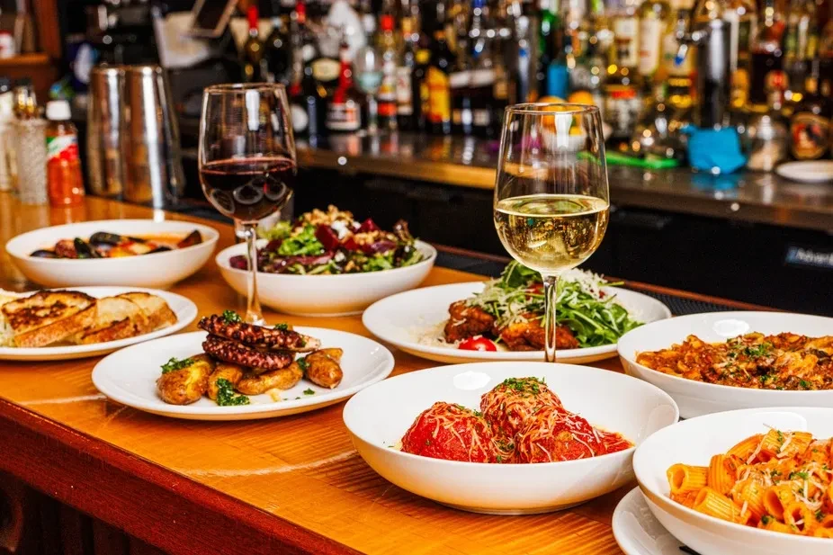 Vibrant spread of grilled octopus, pasta, meatballs, salad, and wine.