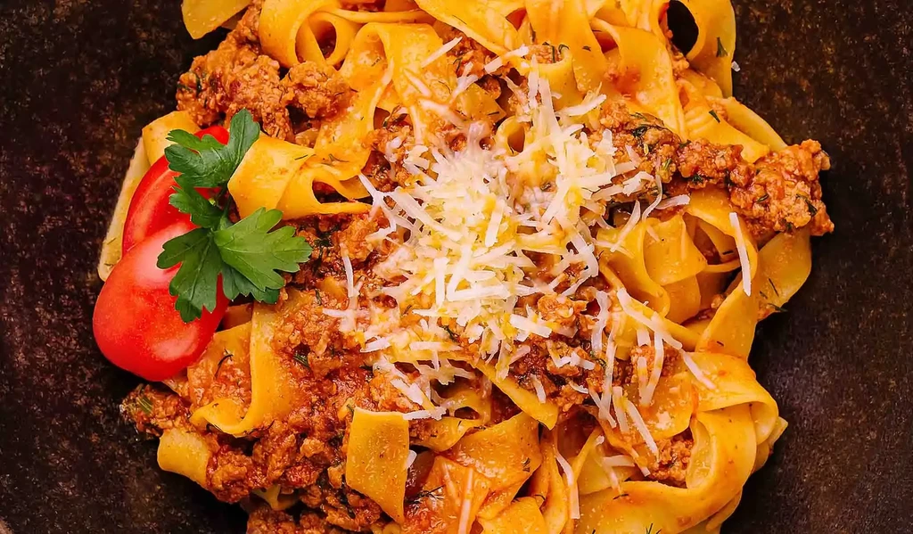 Pappardelle pasta with meat ragu, Parmesan, tomato, and parsley.