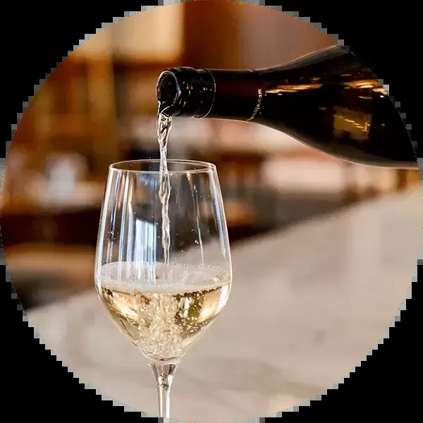 A dark bottle pours effervescent wine into a clear stemmed glass.