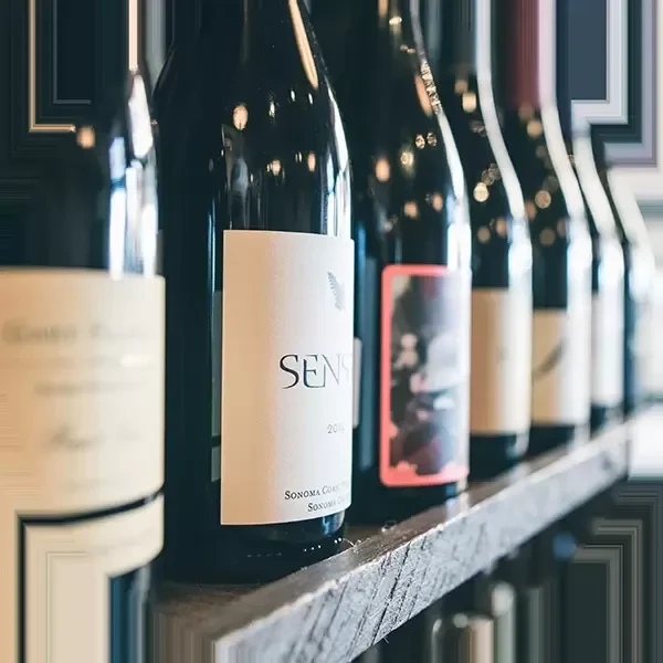 Dark wine bottles on a wood shelf, 'SENS Sonoma Coast' label prominent.