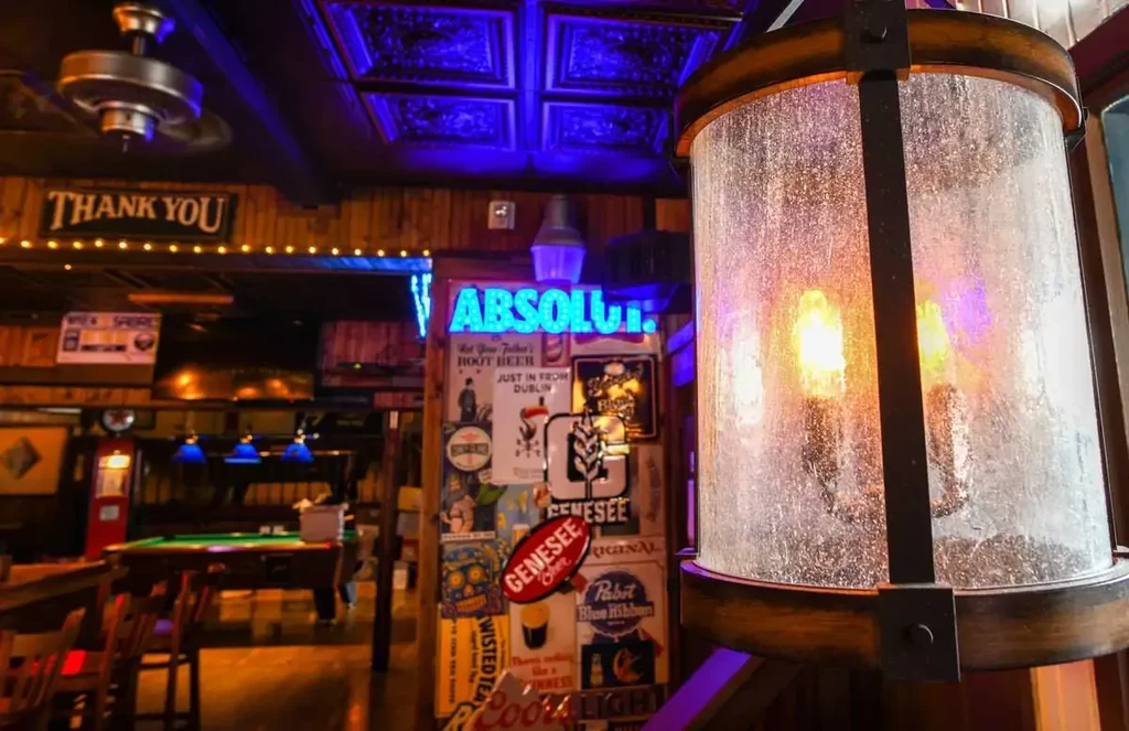 Rustic bar interior with glowing lantern, neon signs, and pool table.
