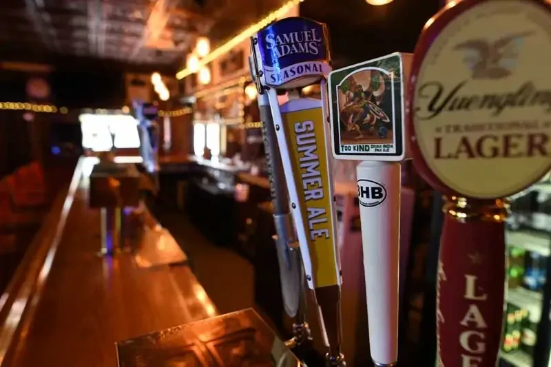 Three beer taps: Samuel Adams, TOO KIND, Yuengling at a dim bar.