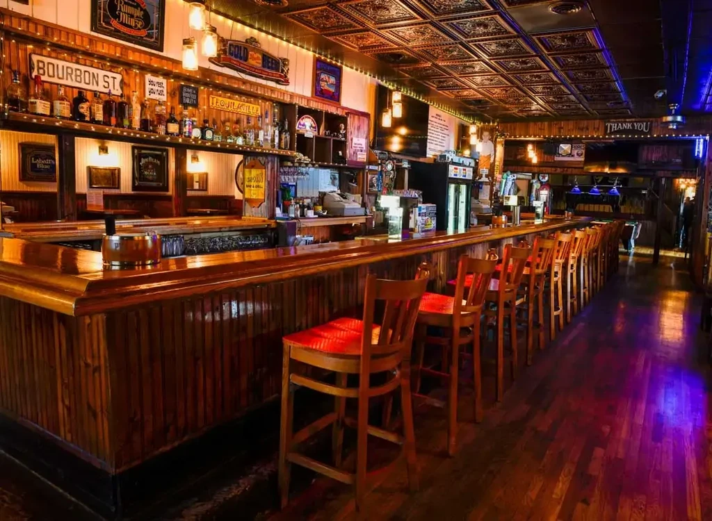 Cozy, empty pub interior with long wooden bar and illuminated bottle display.