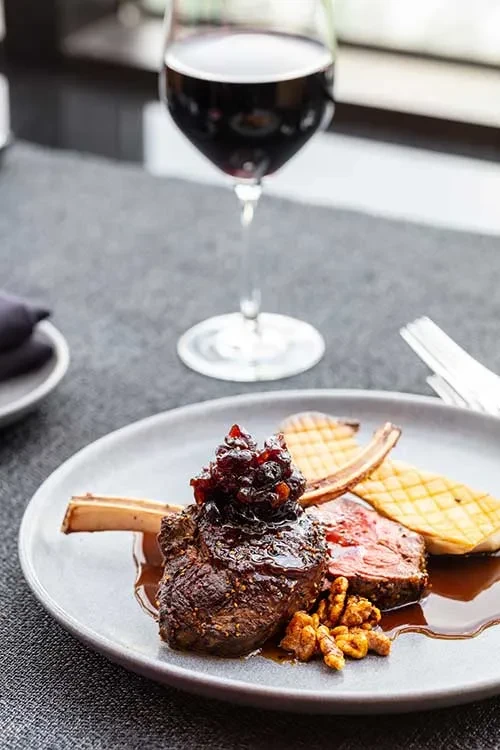 Plated meat chop with berry compote, walnuts, roasted vegetables, red wine.