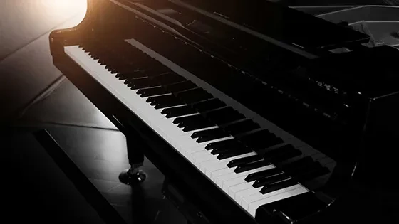 Angled black grand piano, brightly lit, showing keys and reflective body.