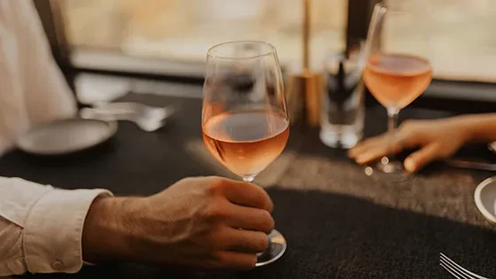 Close-up: two hands, two rosé wine glasses on a dark table.