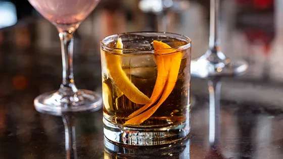 Amber cocktail in a rocks glass with ice and orange peel garnish.
