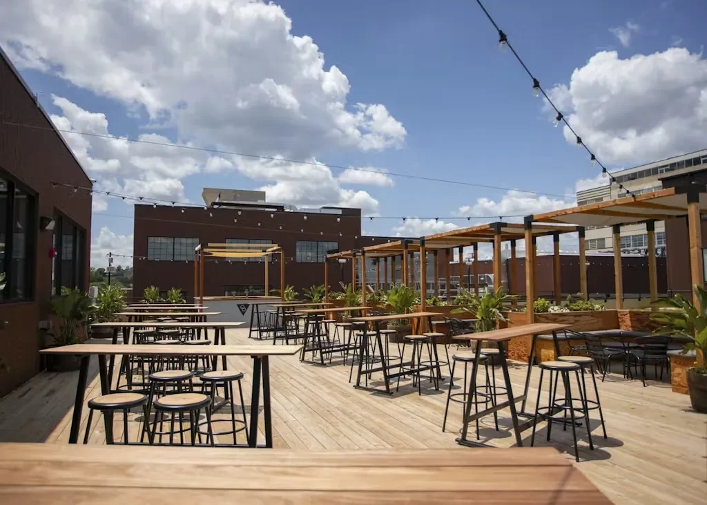 Rooftop patio with high-top tables, bar, pergolas, and string lights.