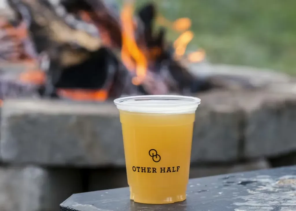 Hazy beverage in "OTHER HALF" cup, background of roaring outdoor fire.