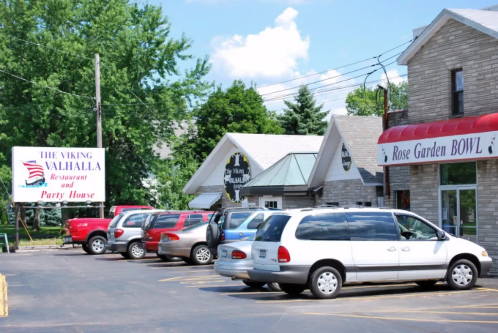 Sunny exterior of Viking Valhalla Restaurant and Rose Garden Bowl with cars.