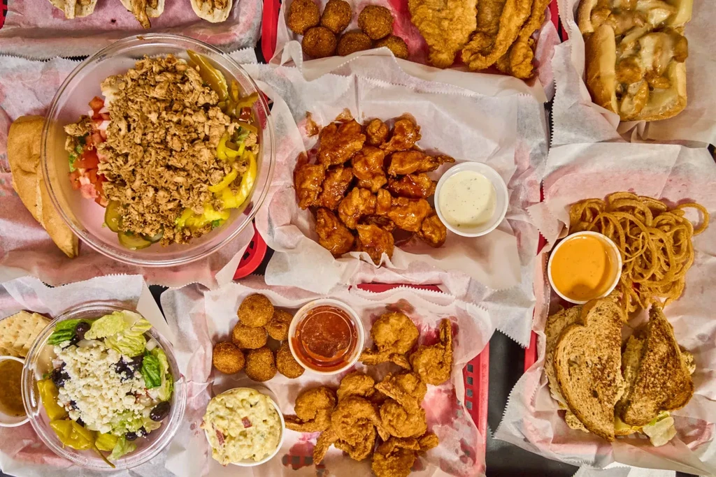 Diverse fried foods, salads, and sandwiches arranged in red plastic baskets.