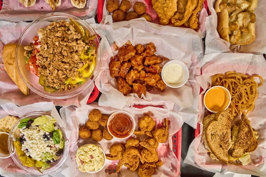 Overhead of salads, fried food, sandwiches in red baskets and clear bowls.